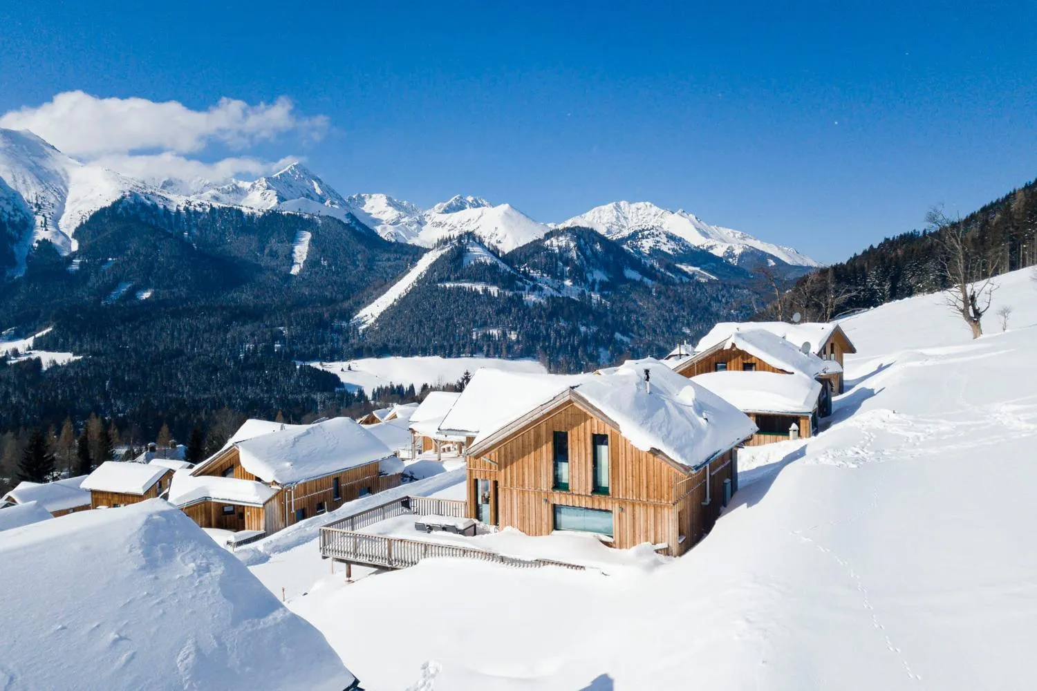 Holzchalets im Schnee mit Panorama auf schneebedeckte Berggipfel