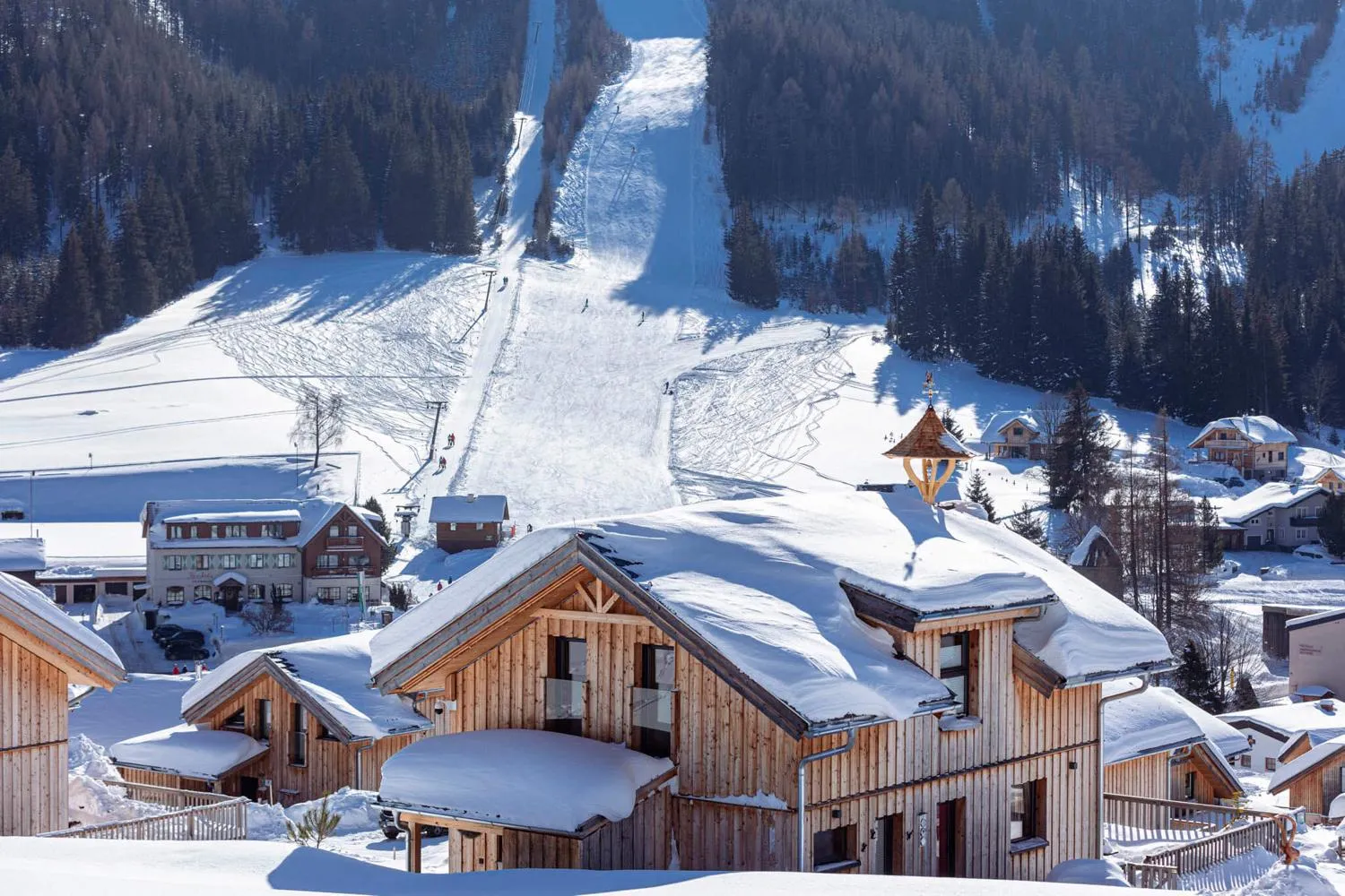 Resort mit Holzchalets vor Skipisten und Berglandschaft im Winter