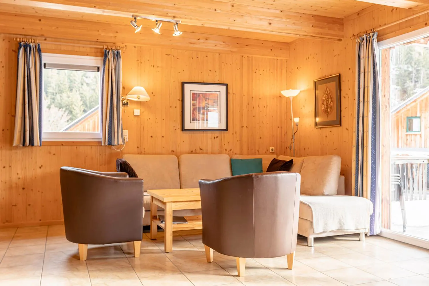 Wohnzimmer mit braunen Ledersesseln, Holzwänden und Balkonblick