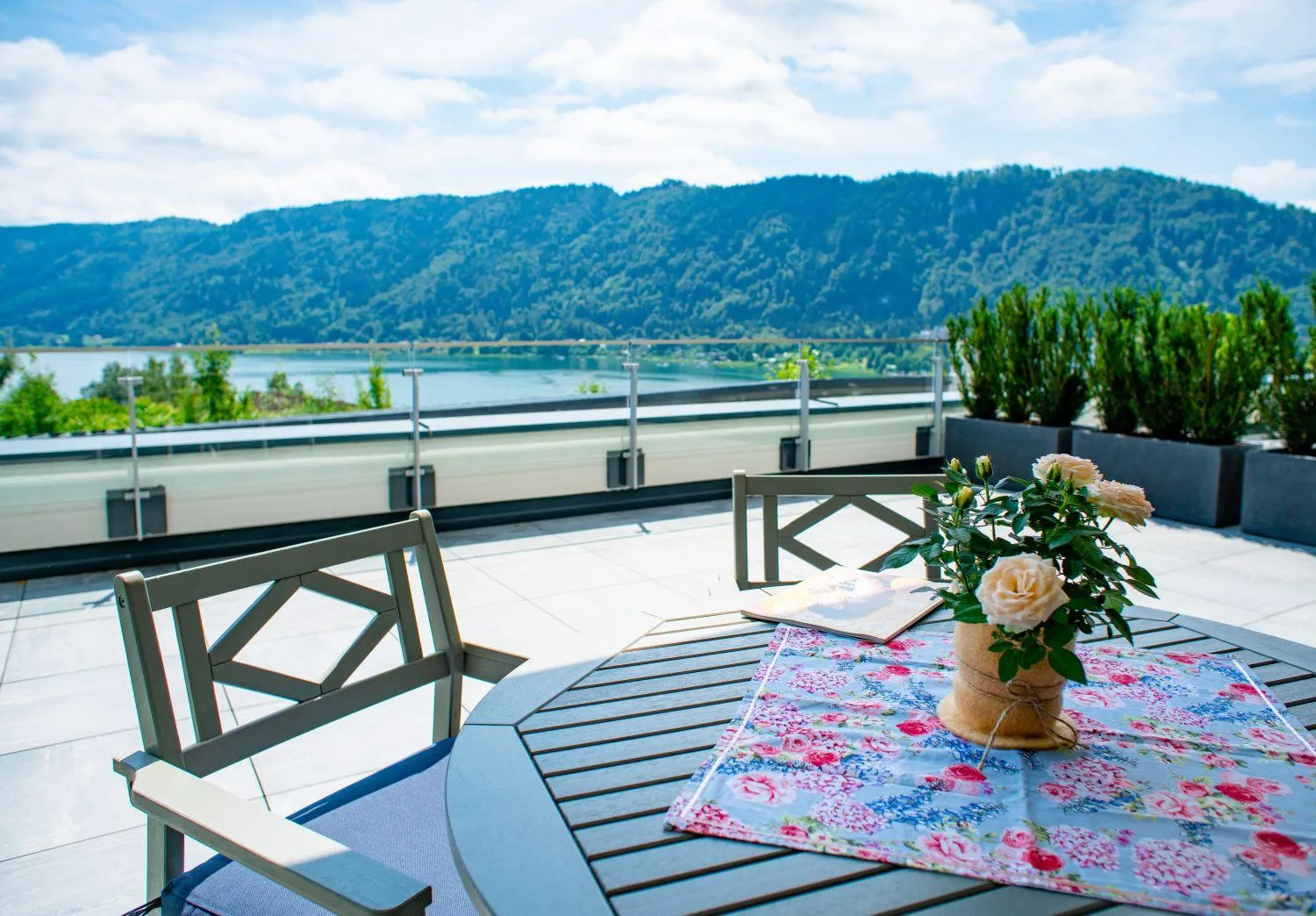 Sonnige Terrasse mit Tisch und Ausblick auf See sowie Berglandschaft