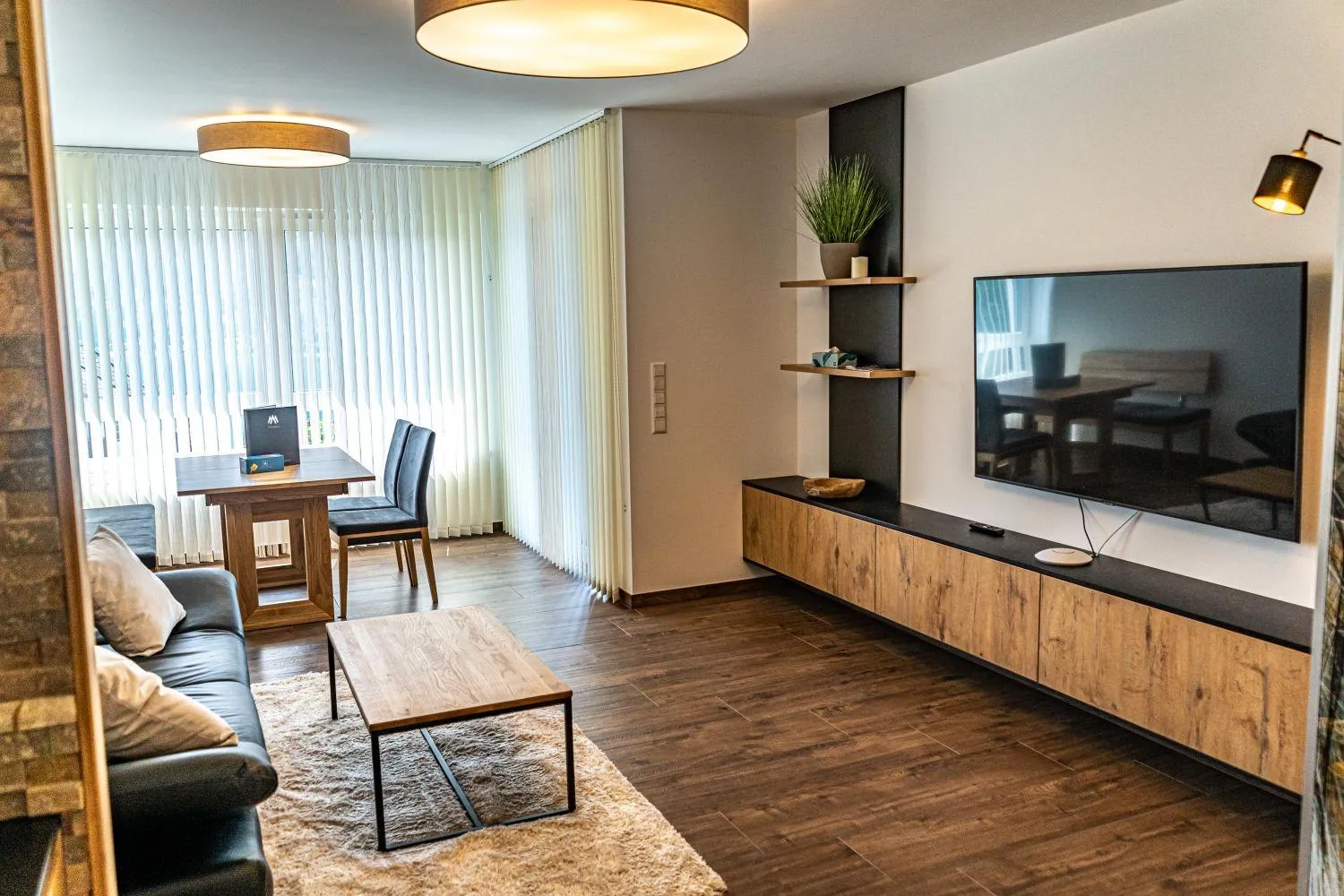 Modernes Wohnzimmer mit TV, Schreibtisch und hellen Fenstern