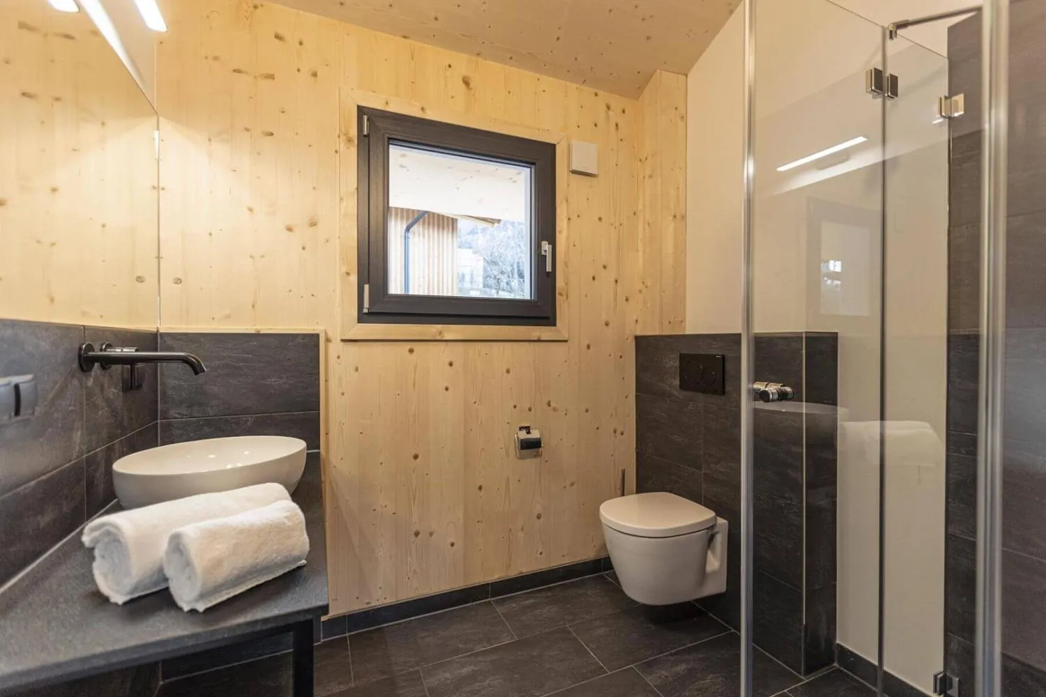 Modernes Badezimmer mit Holzwänden, dunklen Fliesen und Fensterblick