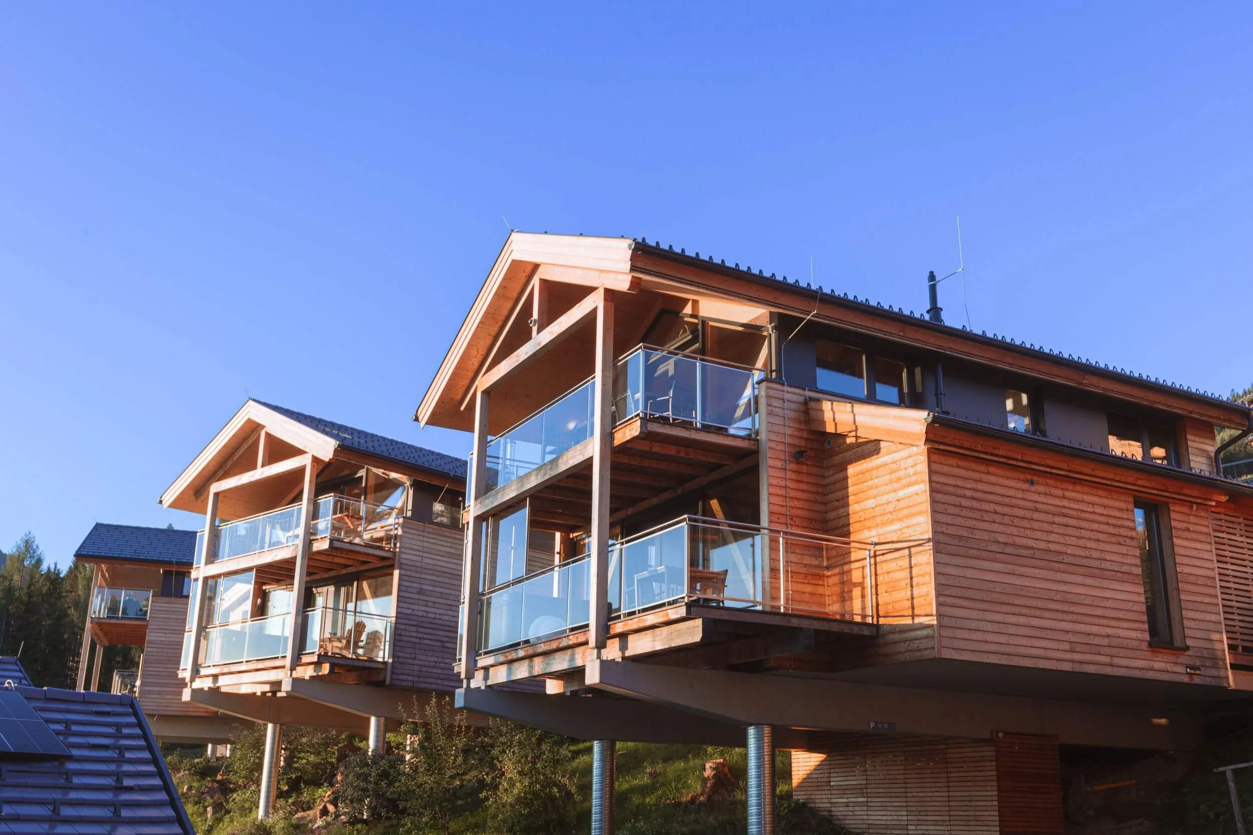 Holzchalets auf Stelzen mit Glasbalkonen am Hang