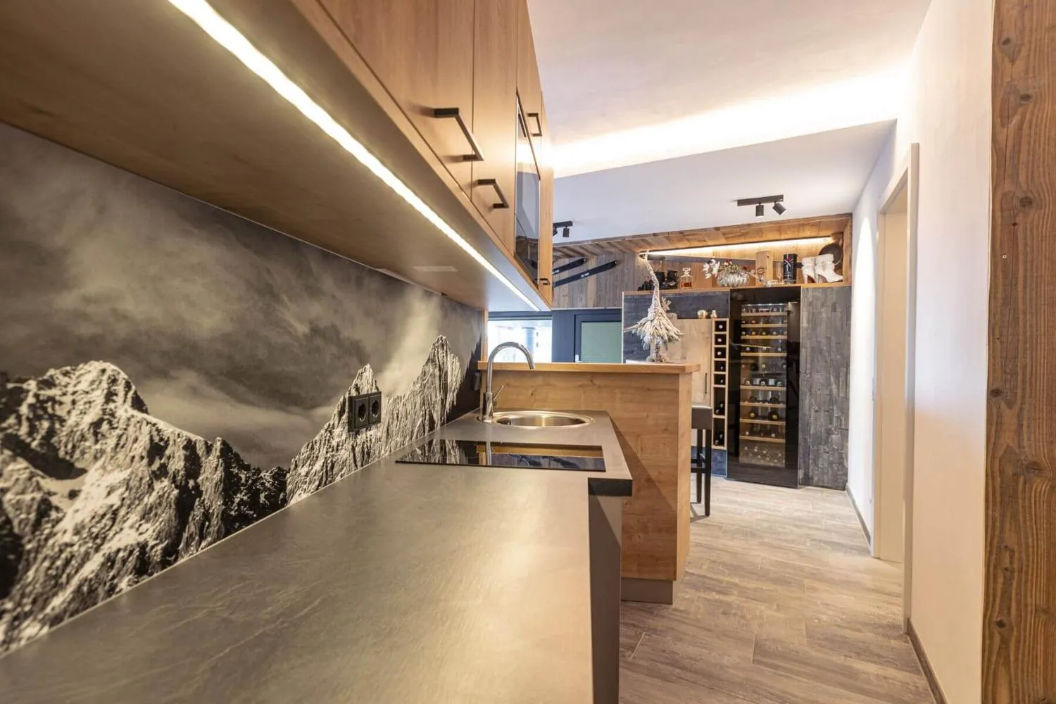 Küche mit Bergmotiv-Wandbild und offenem Blick zur Weinvitrine