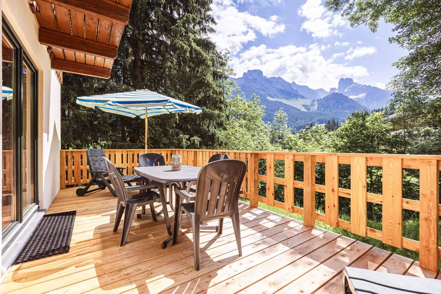 Holzterrasse mit Esstisch, Schirm und Alpengipfeln im Horizont