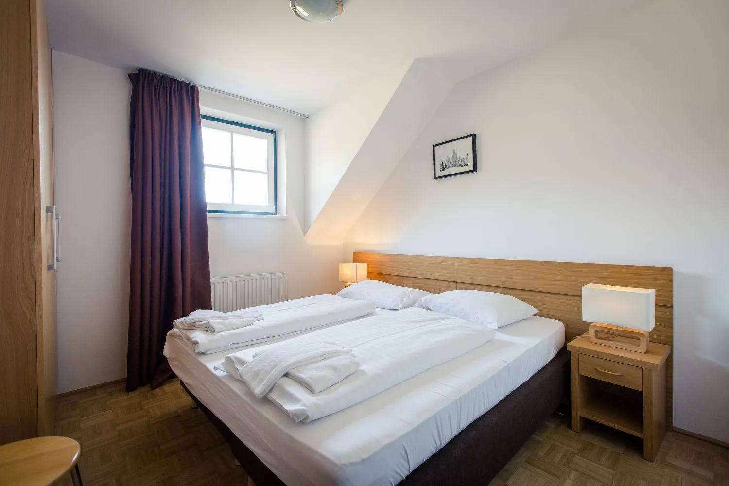 Dachzimmer mit Doppelbett, weißer Bettwäsche und Dachschräge