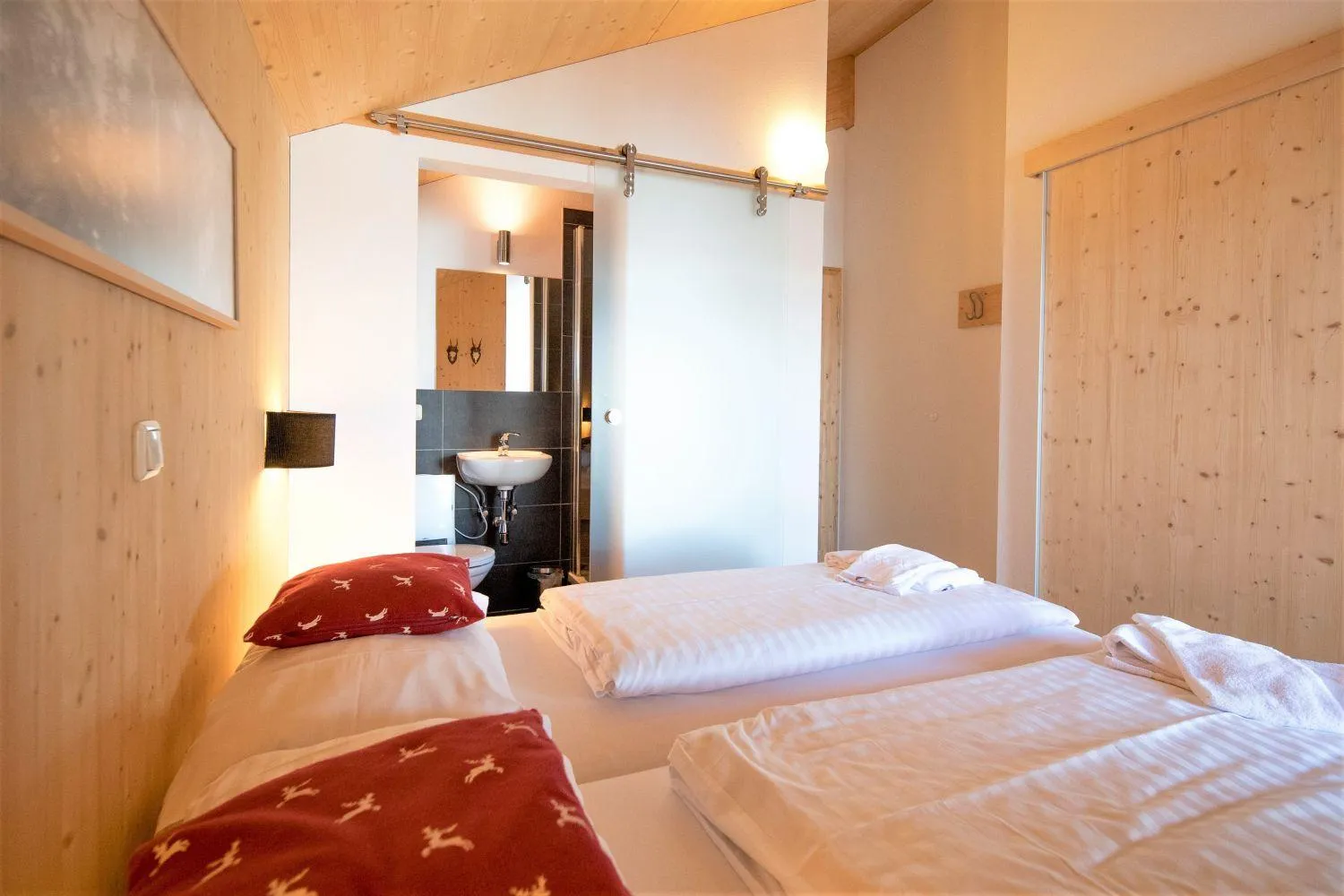 Holz-Schlafzimmer mit zwei Betten, roten Hirschkissen und en-suite Bad
