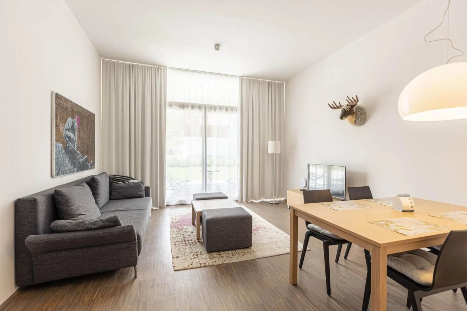 Wohnzimmer mit grauem Sofa, Esstisch und moderner Pendelleuchte