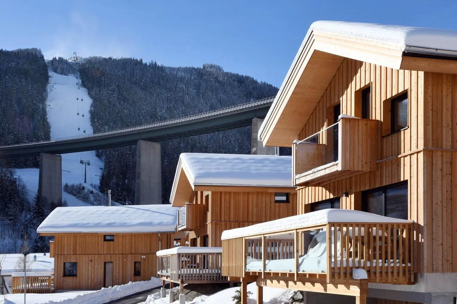 Schneebedeckte Bergalm-Chalets mit Skipiste und Autobahn-Viadukt