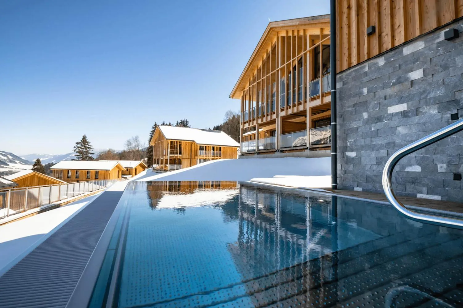 Beheizter Pool im Schnee mit Holzgebäude und Bergpanorama