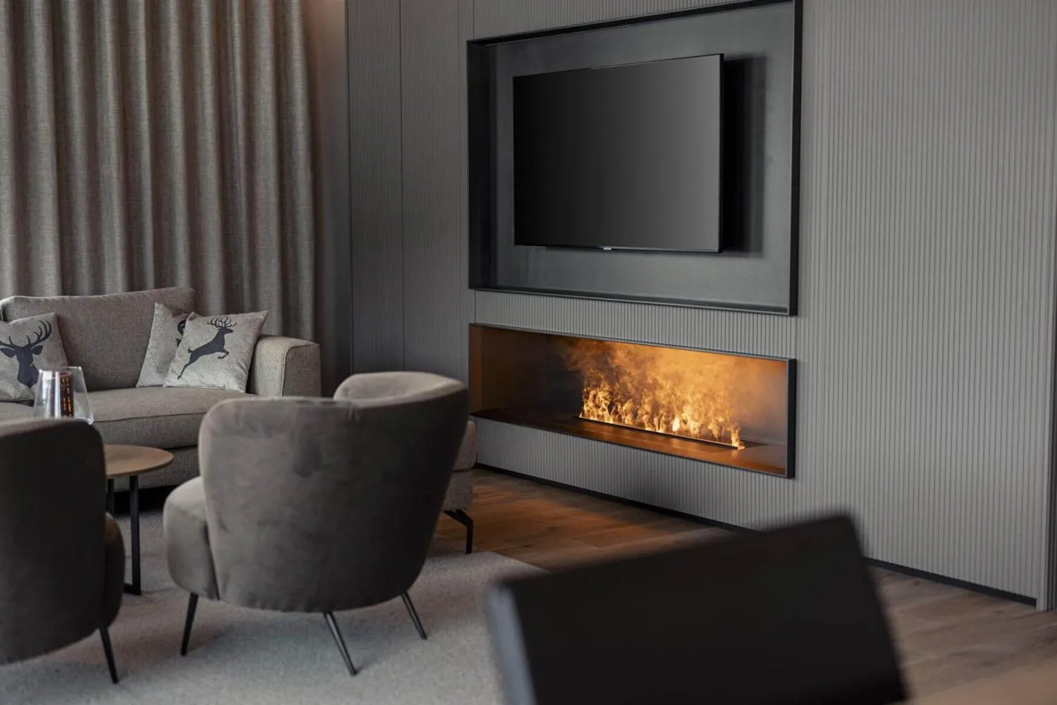 Wohnbereich mit Sessel, Fernseher und brennendem Elektrokaminofen