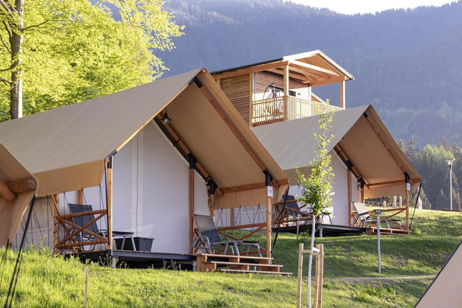 Weiße Glamping-Zelte mit Holzterrassen in grüner Berglandschaft