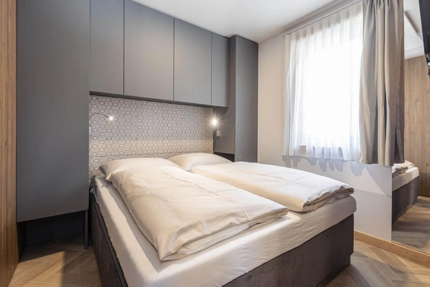 Modernes Doppelzimmer mit grauem Kopfteil und Vorhängen