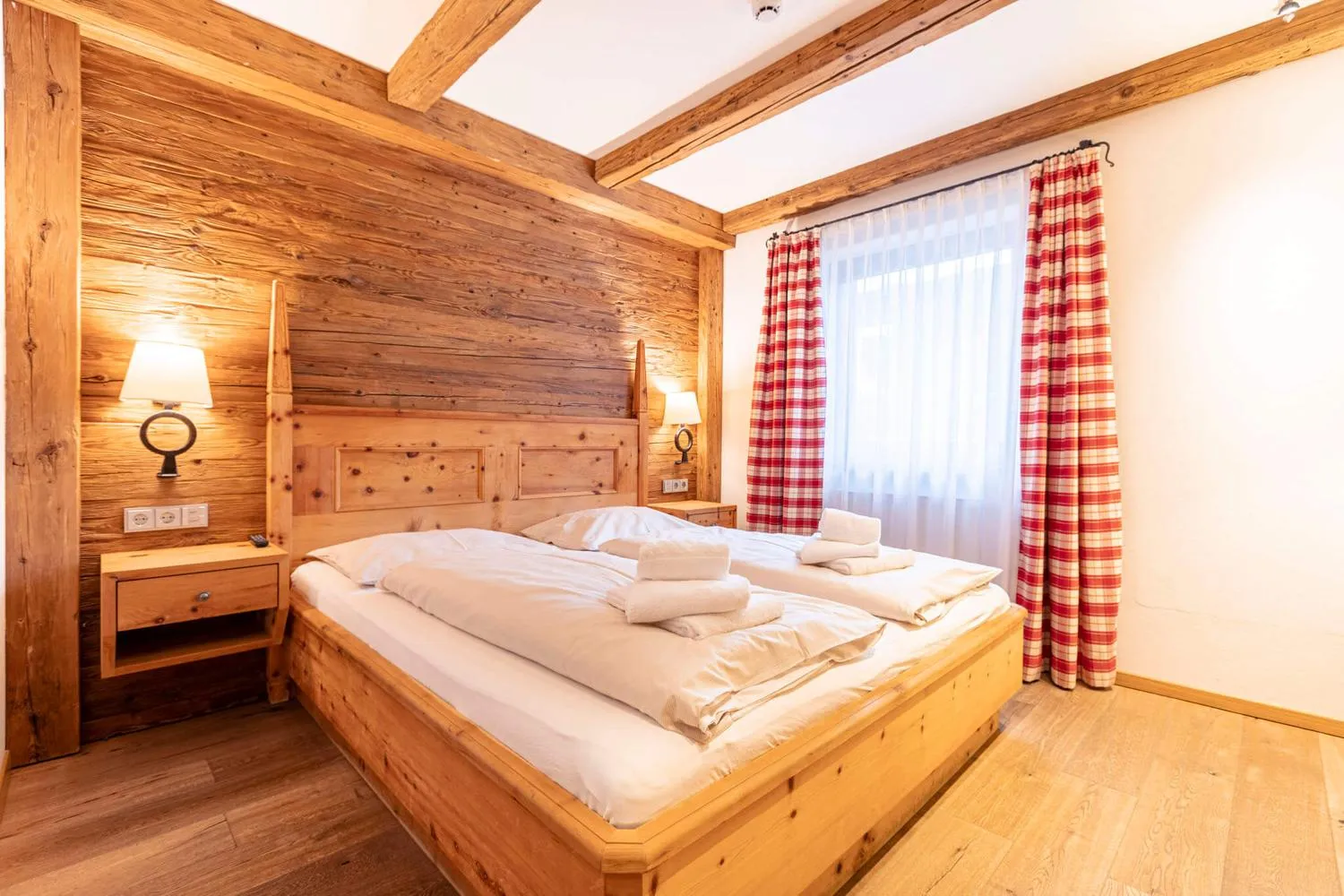 Alpines Schlafzimmer mit Holzbett und kariertem Vorhang