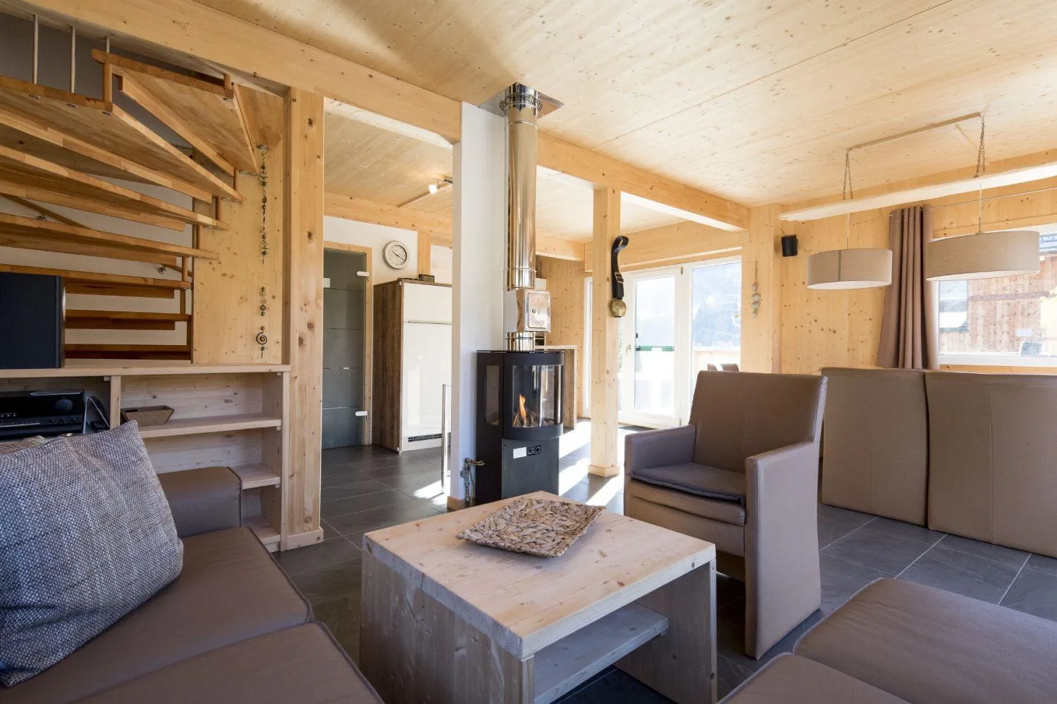 Gemütliches Wohnzimmer mit Kaminofen, braunem Sofa und Holzausstattung
