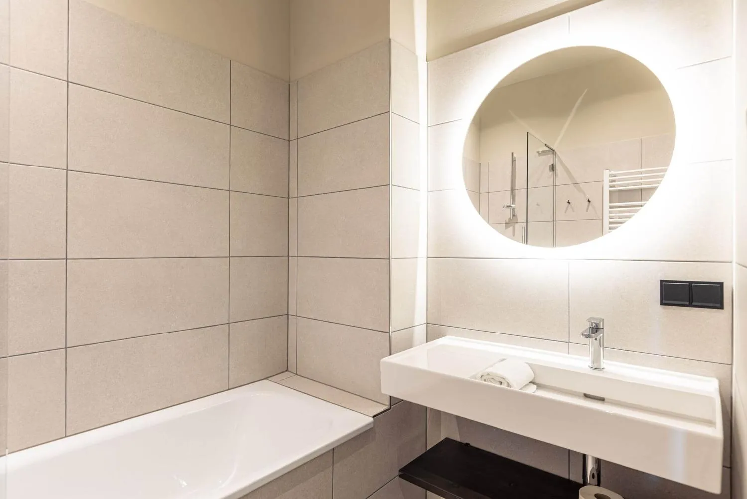 Modernes Badezimmer mit hellem Fliesendesign und runder Spiegel