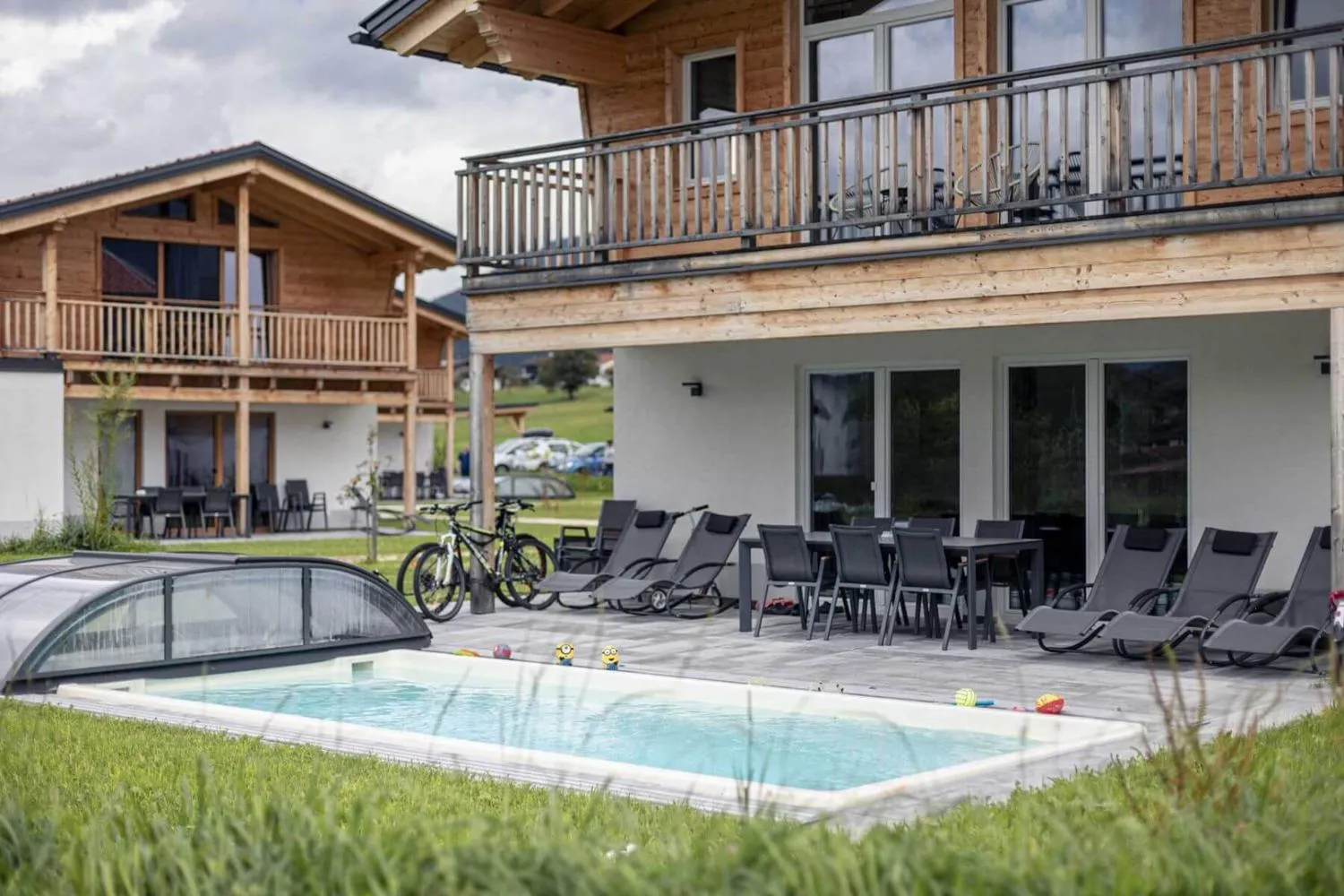 Terrasse mit Pool, Liegestühlen, Esstisch und Fahrrädern vor Chalets