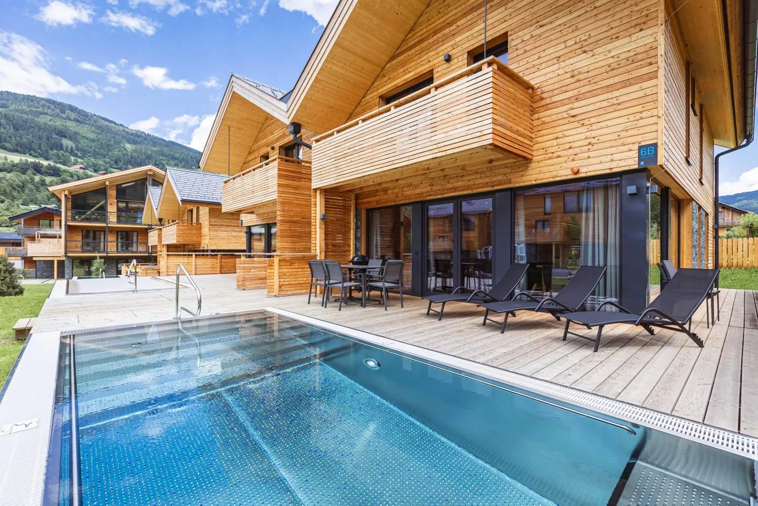 Beheizter Außenpool mit Holzveranda, Liegestühlen und Bergtalblick