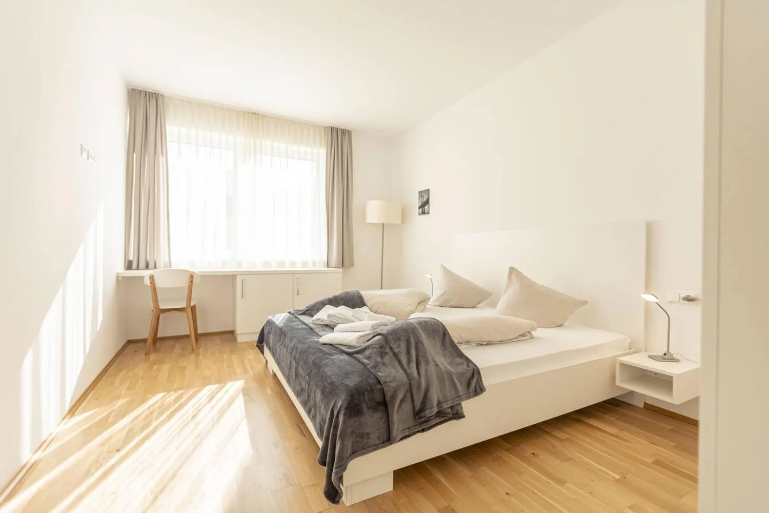 Schlafzimmer mit Holzbett, Schreibplatz und großem Fenster