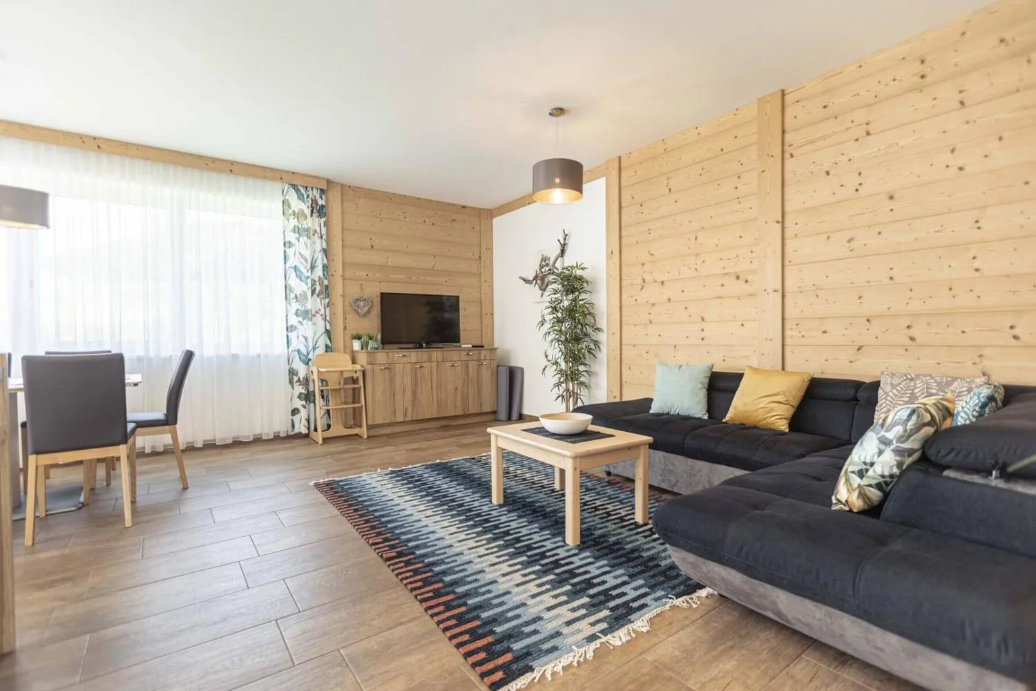 Wohnbereich mit schwarzem Sofa, Holzwänden und Fernseher