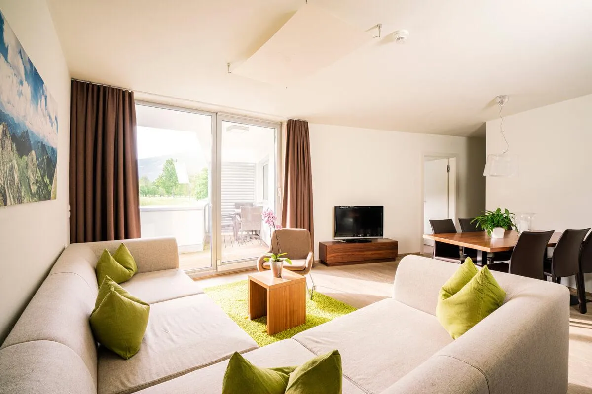 Geräumiger Wohnraum mit hellen Sofas, grünen Kissen und Bergblick