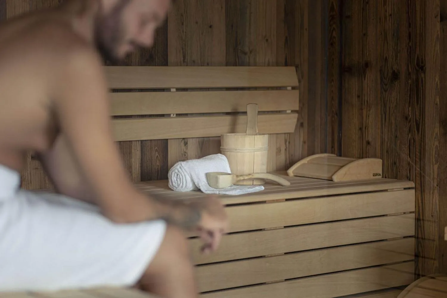 Holzsauna mit Holzbank, Eimer und weißem Handtuch