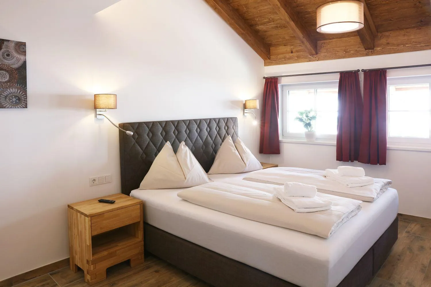 Schlafzimmer mit Doppelbett, Holzdecke und bordeauxfarbenen Vorhängen
