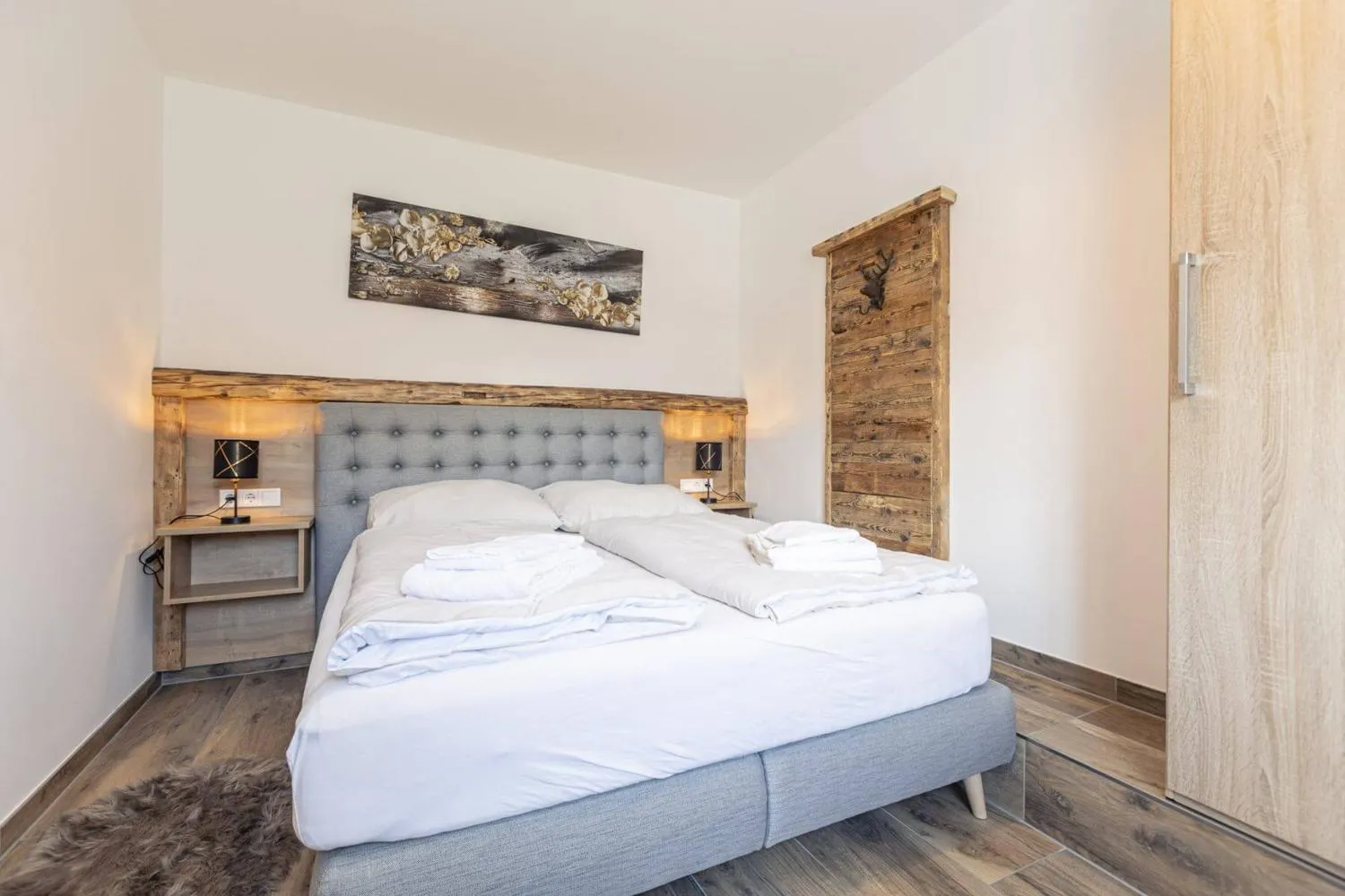 Schlafzimmer mit grauem Bett, Holzrahmen und Kleiderschrank