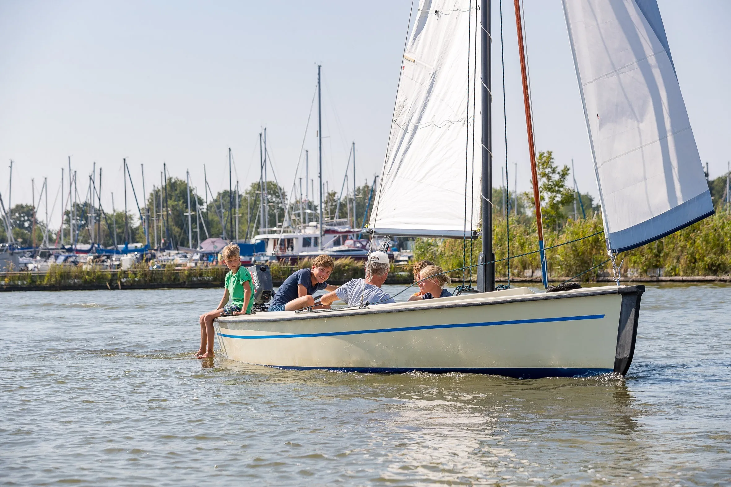 Offene Segeljolle mit vier Personen an Bord vor den Masten des Yachthafens