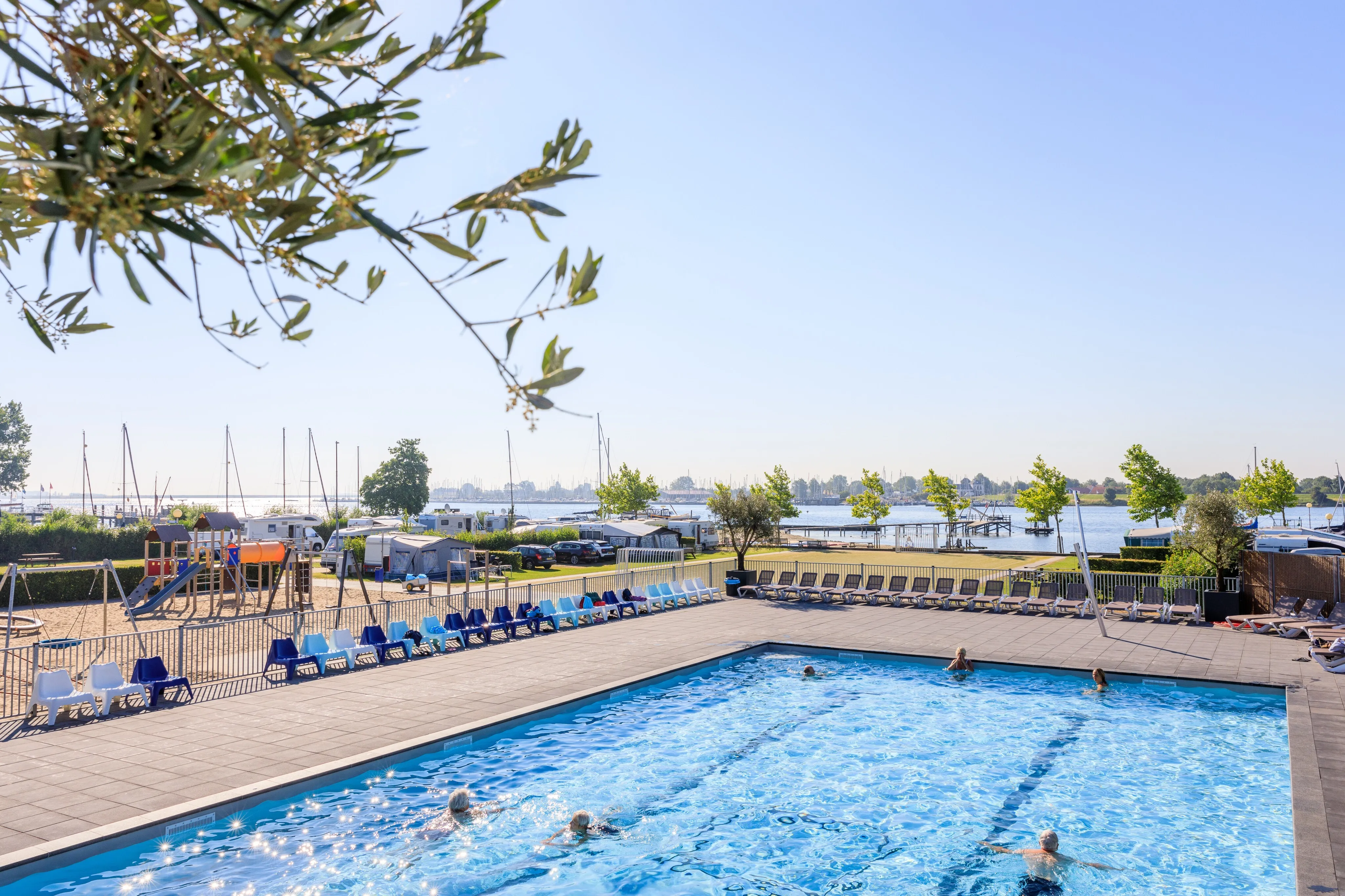 Freibad mit Schwimmern und Liegestuhlreihe, dahinter der Yachthafen am Veerse Meer
