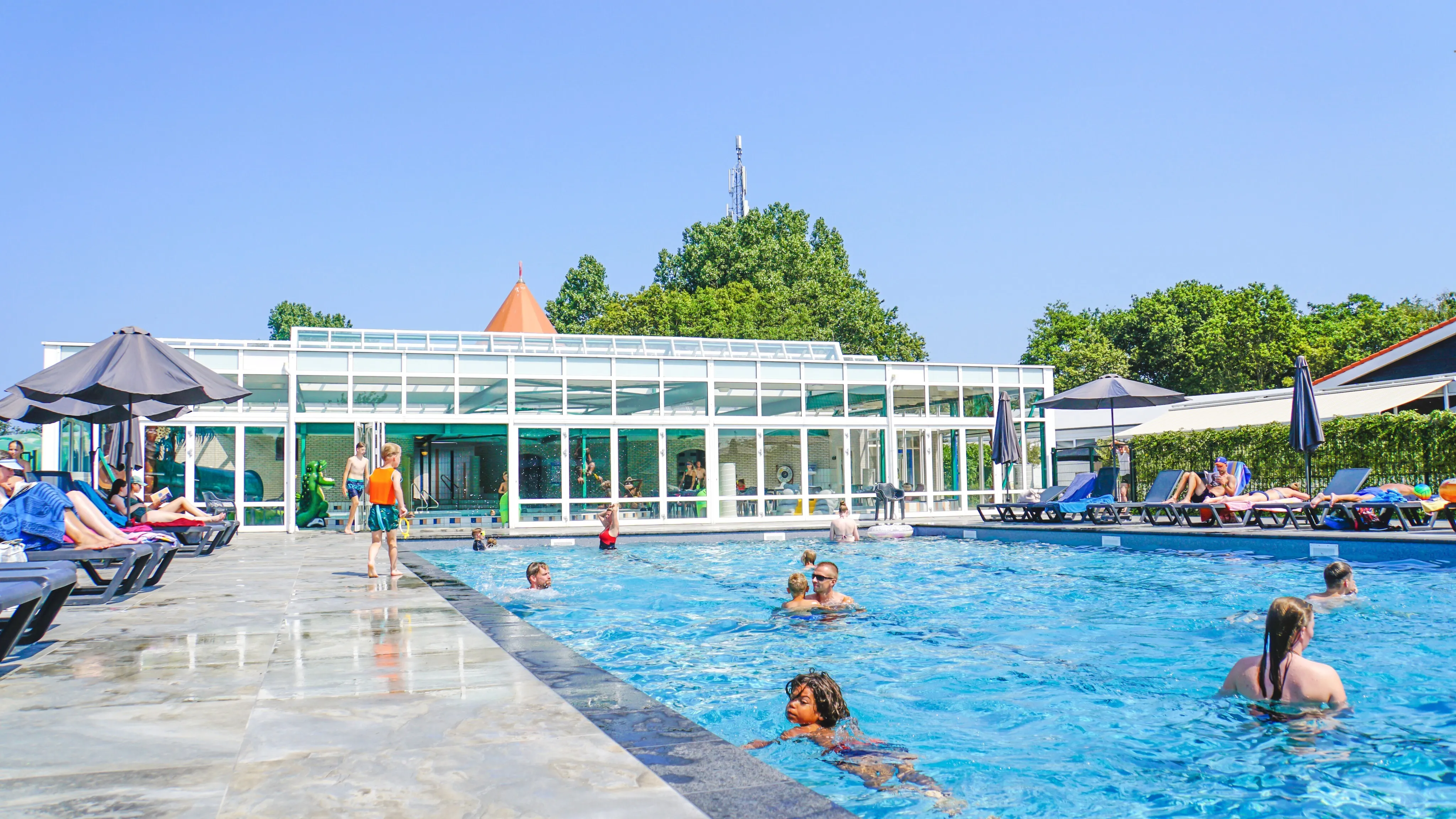 Freibad mit Liegestühlen und Sonnenschirmen vor dem verglasten Badegebäude