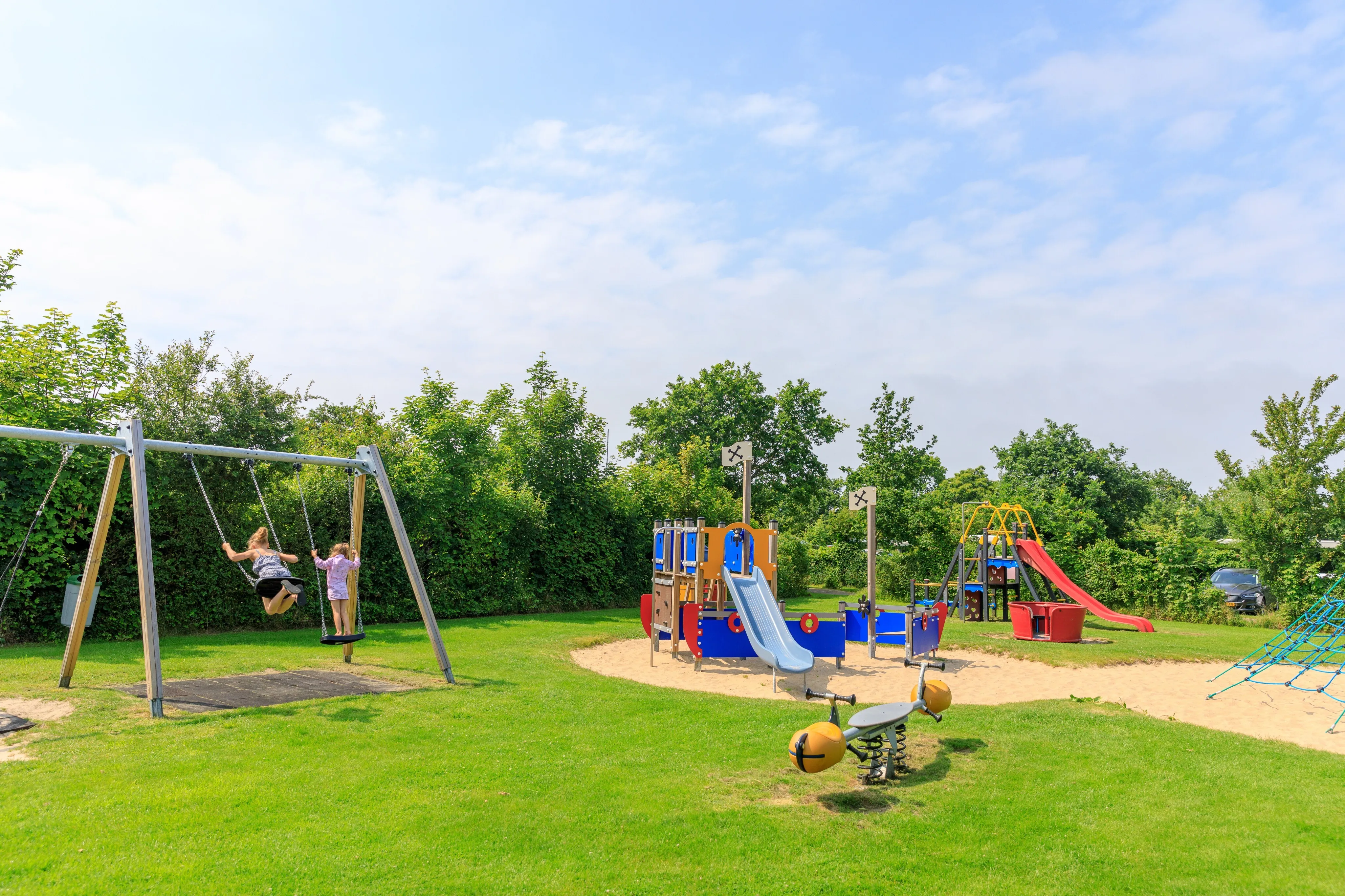 Spielplatz mit Schaukel, Kletterturm und zwei Rutschen auf der Wiese