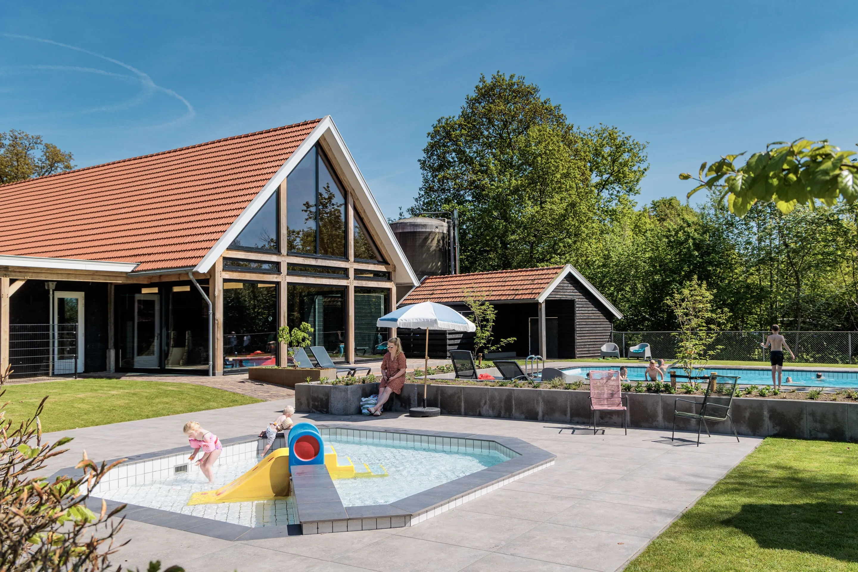 Planschbecken mit gelber Kleinkinderrutsche vor dem Badegebäude, dahinter das Schwimmbecken