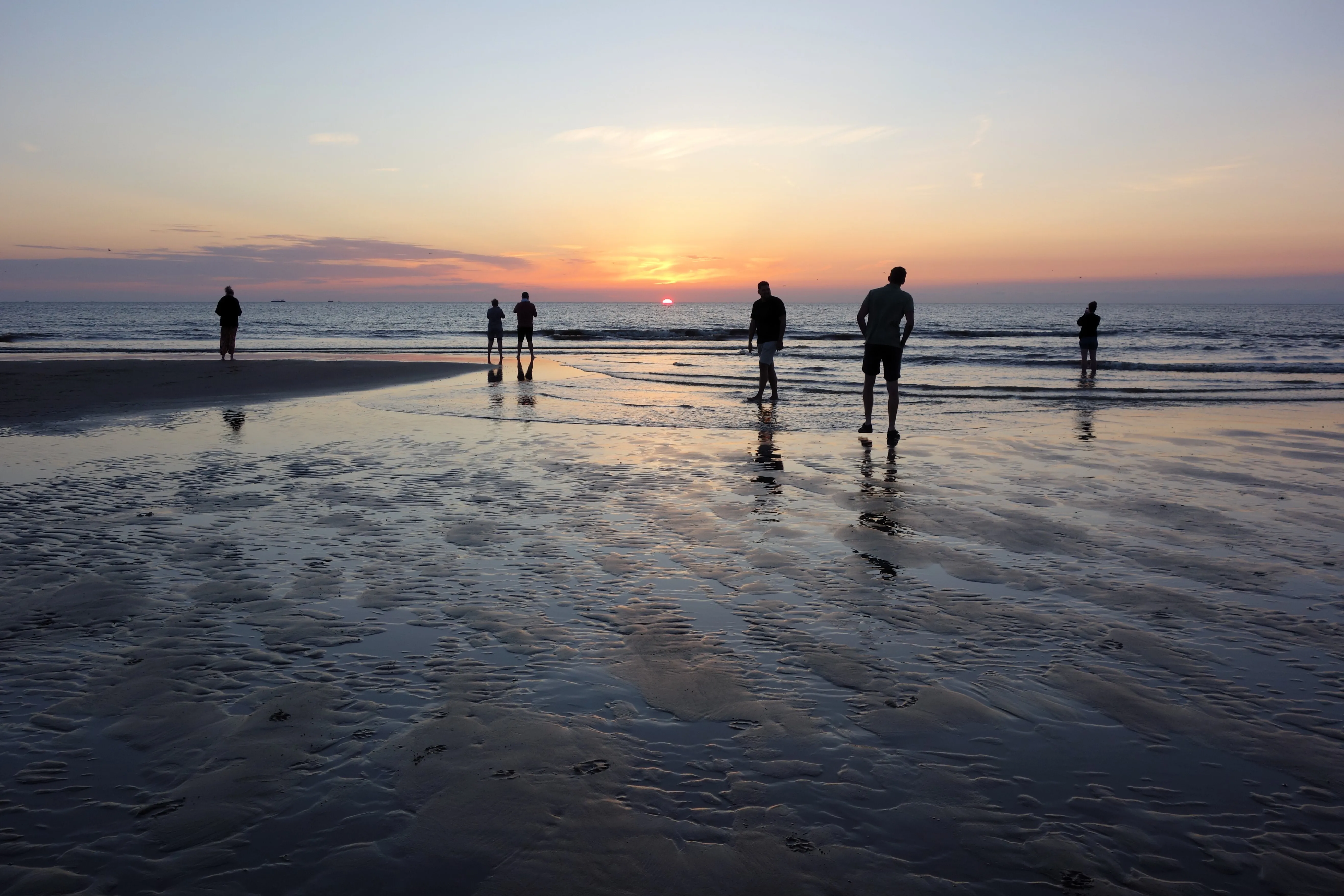 Spaziergänger auf dem nassen Sandstrand bei Sonnenuntergang über der Nordsee