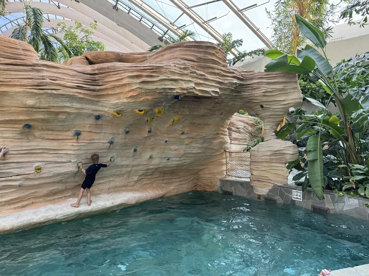 Holzkletterwand mit farbigen Griffen, Kind beim Erklettern im Innenbad