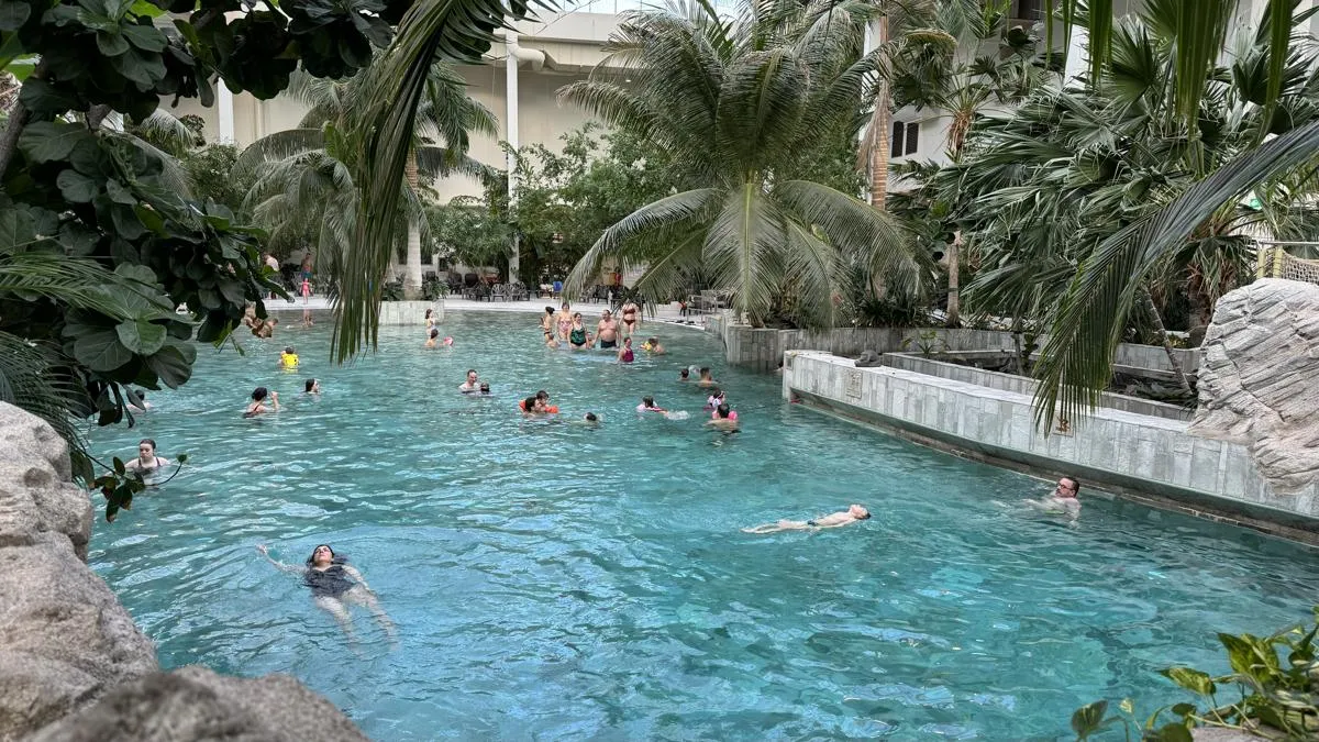 Innen-Wellenbad mit türkisem Wasser, Palmen und zahlreichen Besuchern