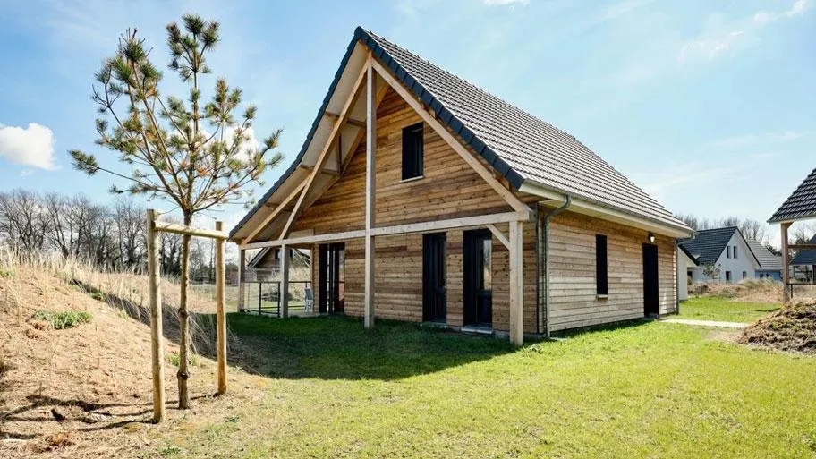 Modernes Holzhaus mit großem Giebeldach und überdachter Veranda in grüner Umgebung