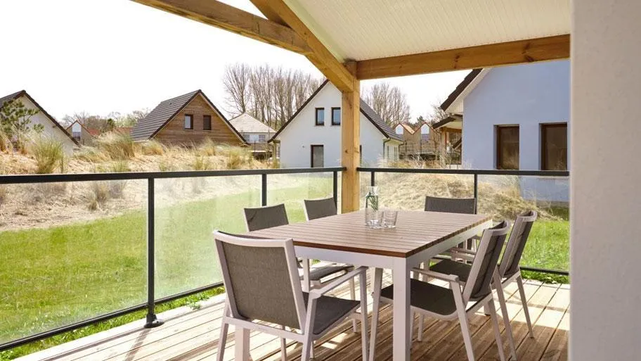 Gedeckter Tisch mit vier Stühlen auf Holzterrasse mit Ausblick auf Rasenfläche