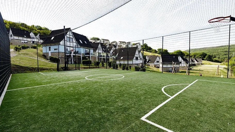 Überdachter Futsal-Platz mit grünem Kunstrasen und Ferienpark-Häusern