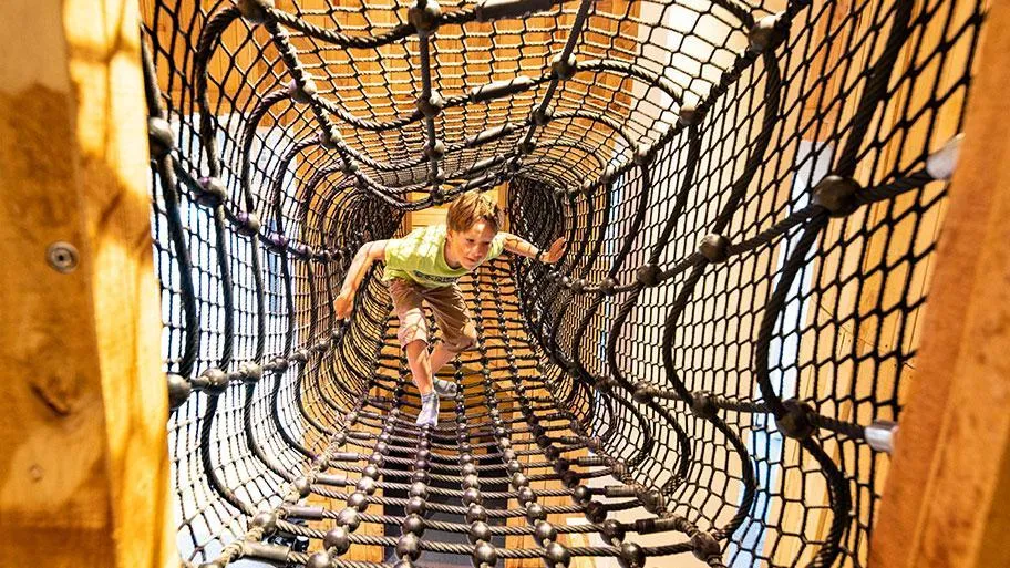 Kind klettert durch Netz-Tunnel im Spielgerät des Freizeitbereichs