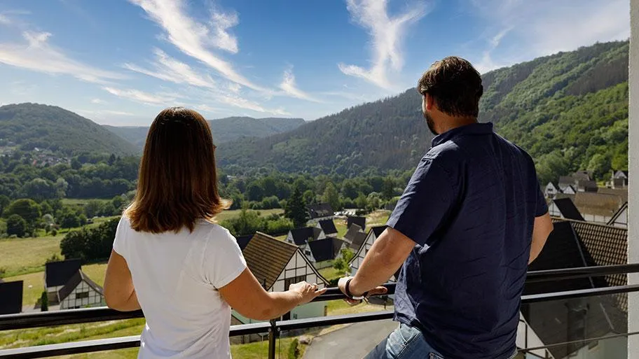 Paar genießt Ausblick auf waldige Eifelhügel vom Balkon
