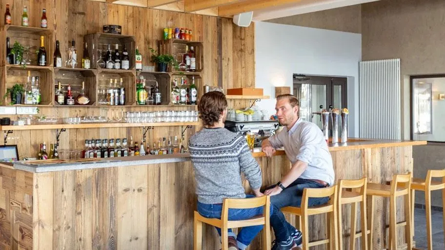 Holzbar mit Gästen, Flaschenregalen und warmer Innenbeleuchtung