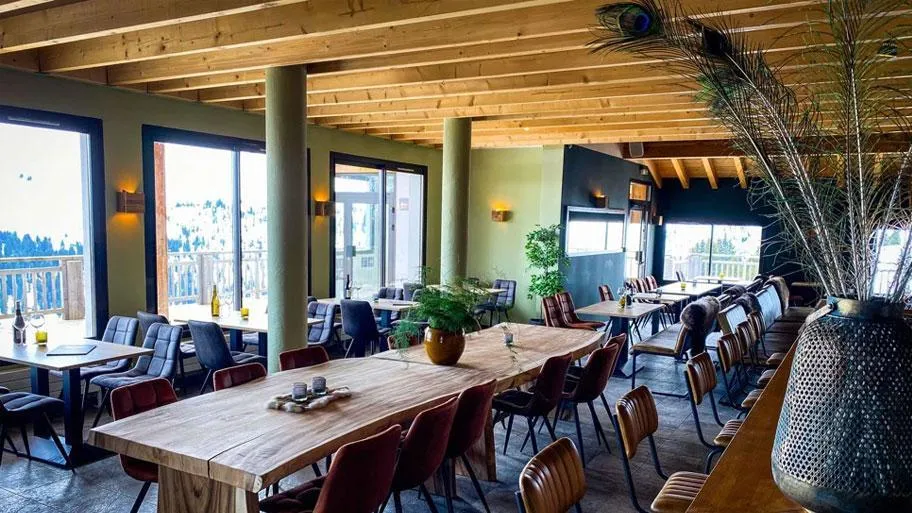 Restaurant mit Holztischen, Stühlen und großer Fensterfront zu Bergen