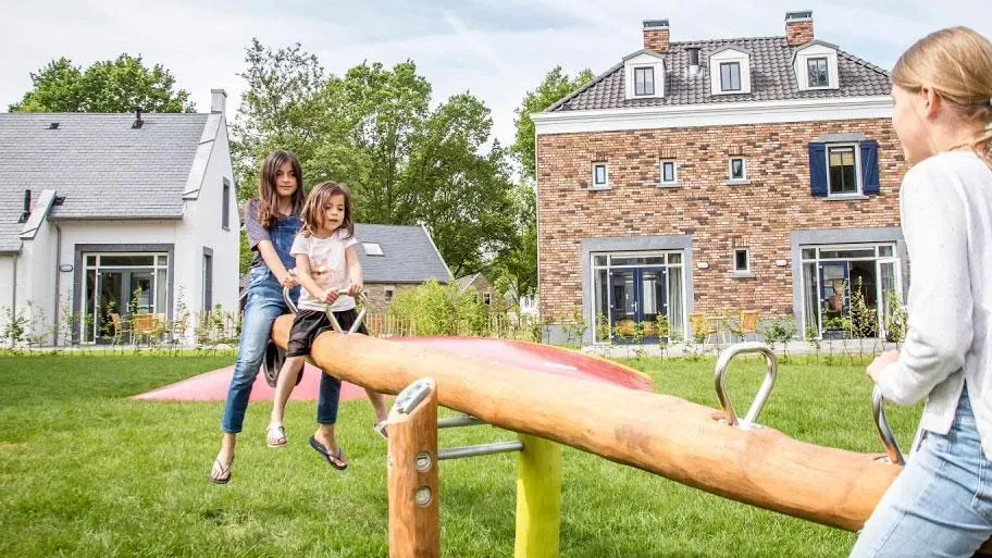 Kinder spielen auf Balkenwaage vor Ferienhäusern