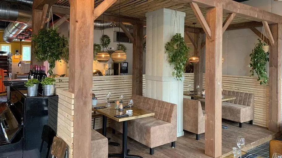 Restaurant mit Holzbalken, gepolsterten Sitzbänken und Grünpflanzen