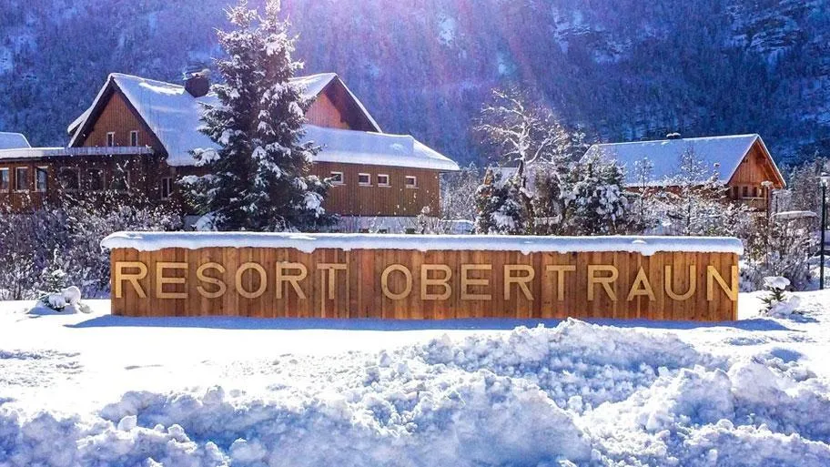 Holzschild Resort Obertraun mit schneebedeckten Chalets und Bergen im Winter