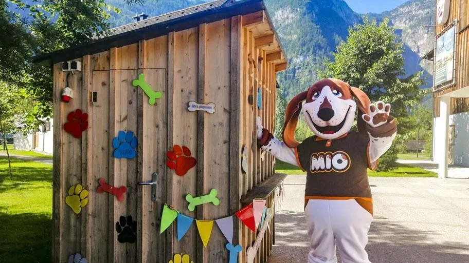 Hölzernes Spielhaus mit Pfotenmotiven und Maskottchen vor Berghang