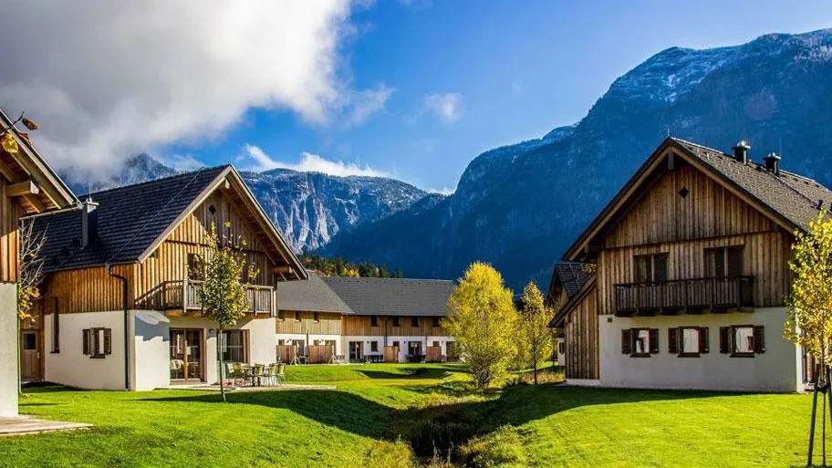 Holzchalets mit weißen Wänden in grüner Landschaft vor Bergkette