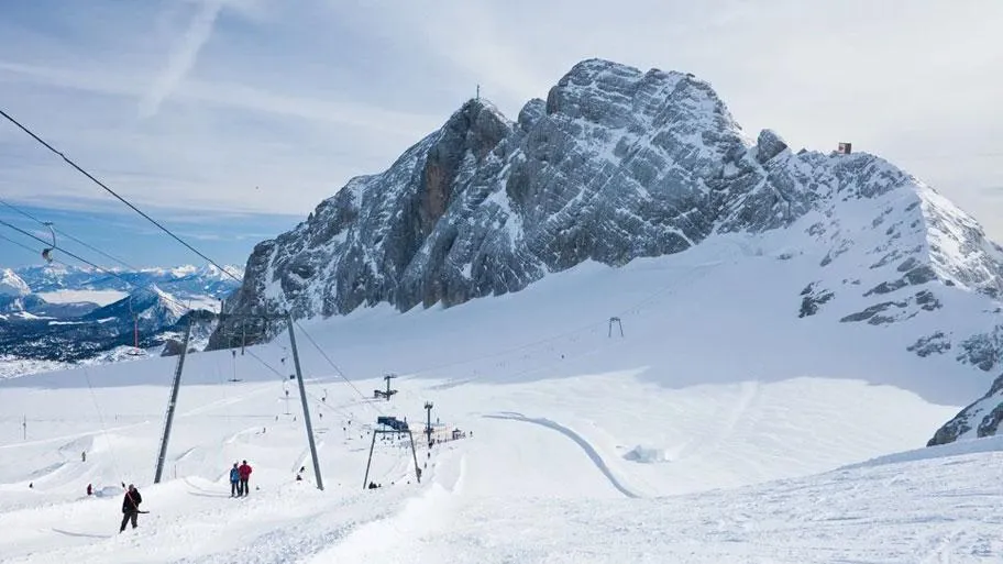Skigebiet mit Skilift und Skifahrern vor schneebedecktem Bergmassiv