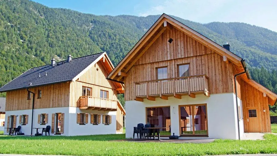 Zwei Chalets mit Holzfassaden und Terrassen vor bewaldeter Bergkulisse